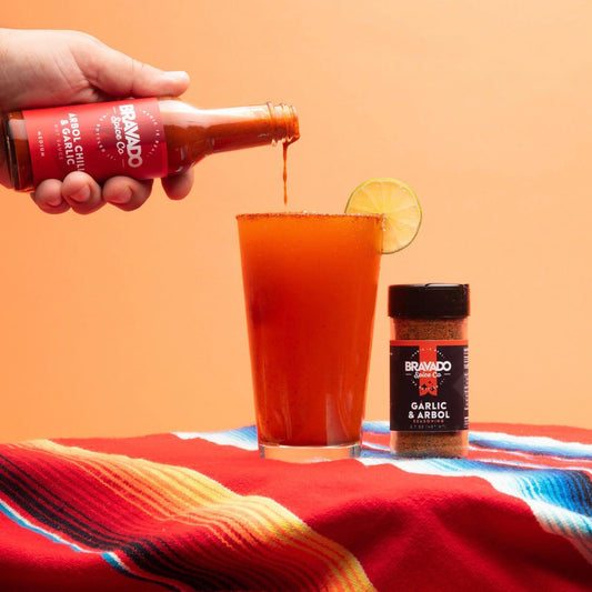 Bravado Spice Co.’s Arbol Chili & Garlic hot sauce poured into a Michelada drink next to Garlic & Arbol seasoning.