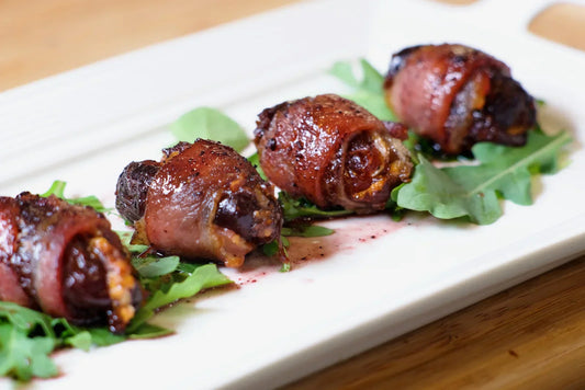 Devils on Horseback (bacon-wrapped dates) plated on fresh arugula with a dark glaze drizzle.