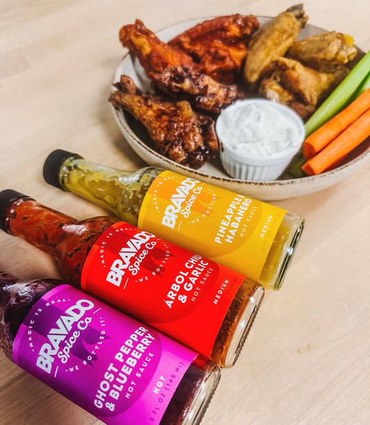 Game day wings on a plate with bottles of Bravado Spice Co’s Hot Sauces beside them.