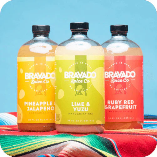 Bravado Spice Co.’s Pineapple & Jalapeño, Lime & Yuzu, and Ruby Red Grapefruit margarita mixers displayed on a blue background.