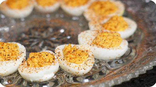 Deviled eggs sprinkled with Bravado spices and served with their hot sauce on a glass plate.